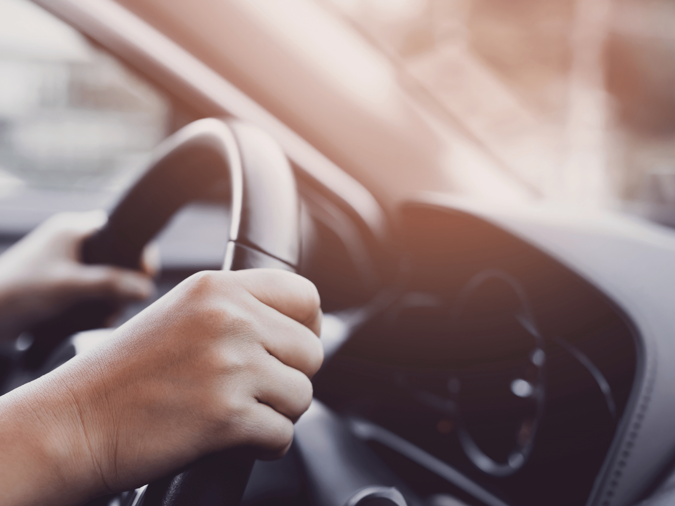 two hands on a steering wheel with a sun burst of light through the windshield