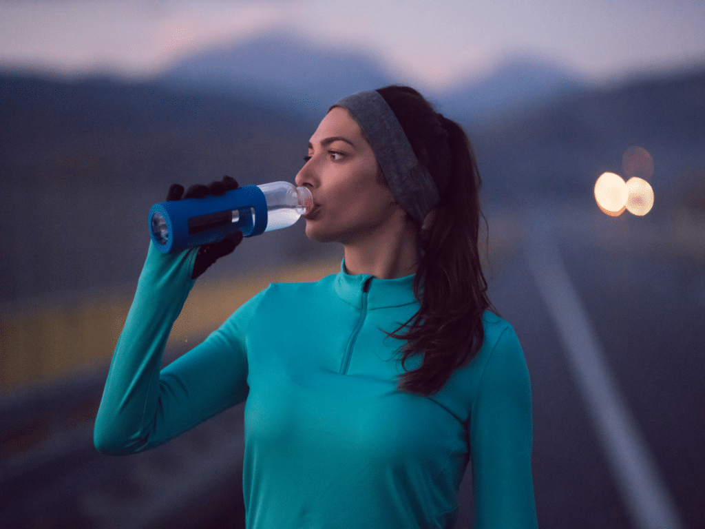 young woman with long dark hair and a teal long sleeved shirt is drinking water out of a water bottle